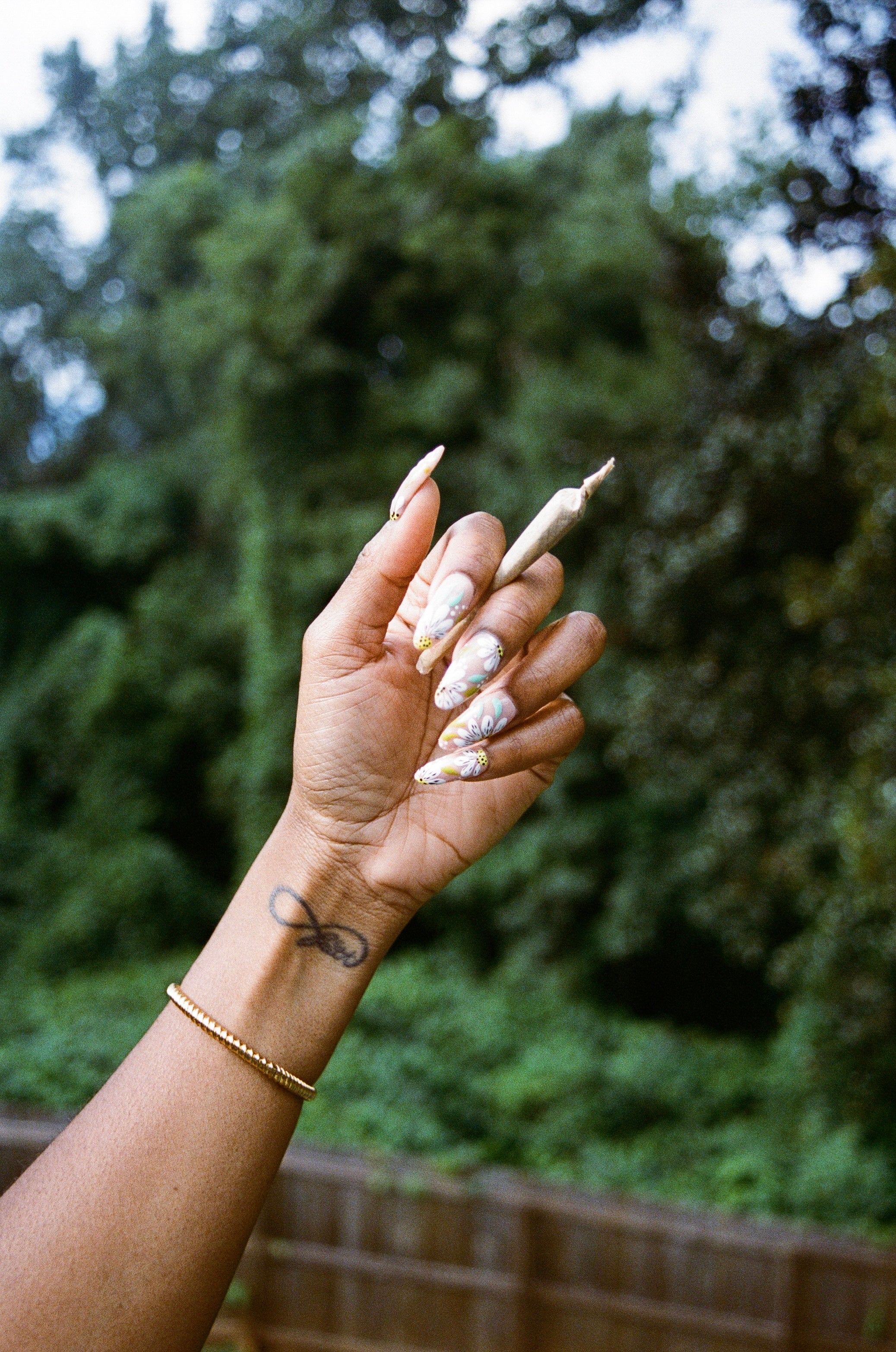 Photo of a Black woman's hand with a joint in between her fingers.